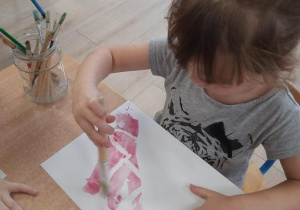 Dziewczynka maluje pędzlem po białej kartce.