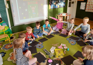 Dzieci siedzą na dywanie, na środku zgromadzone materiały plastyczne