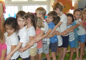 Dzieci dotykają swoich łokci stojąc jeden za drugim.