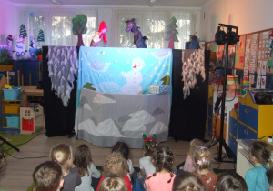 Dzieci oglądają przedstawienie w tle kukiełki Baby Jagi i wilka.