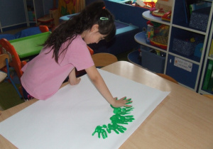 Dziewczynka odciska swoje dłonie umoczone w farbie na kartonie.