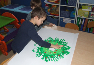 Chłopiec odciska swoje dłonie umoczone w farbie na kartonie.