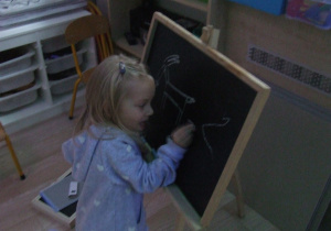 Dziewczynka rysuje kredą na tablicy.