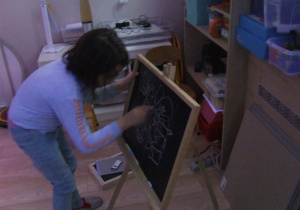 Dziewczynka rysuje kredą na tablicy.