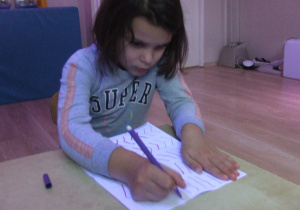 Dziewczynka rysuje szlaczki po śladzie.