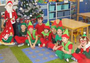 Mikołaj i elfy pozują do zdjęcia przy choince.