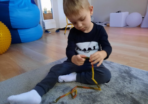 Chłopiec nawleka makaron na sznurek.