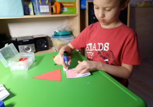 Chłopiec smaruje klejem papier.