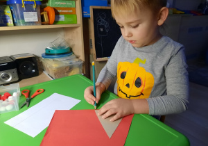 Chłopiec odrysowuje szablon trójkata na czerwonej kartce.
