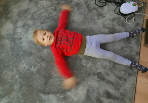 Chłopiec lezy na dywanie i rusza rączkami, wykonuje postać aniołka.