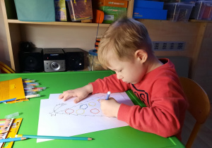 Chłopiec rysuje po śladzie bombki na choince.