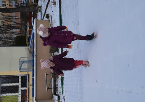 Dziewczynki robią ślady na śniegu na boisku przedszkolnym.