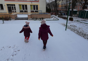 Dziewczynki robią ślady na śniegu na boisku przedszkolnym.