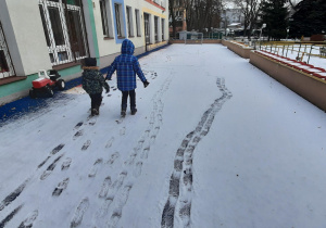 Chłopcy robią ślady na śniegu na tarasie przedszkolnym.