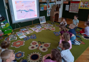 Dzieci oglądają dzieła malarstwa o tematyce zimowej, na tablicy multimedialnej.