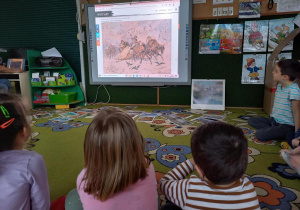 Dzieci oglądają dzieła malarstwa o tematyce zimowej, na tablicy multimedialnej.