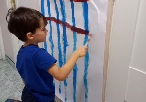 Chłopiec maluje na dużym kartonie, na ścianie