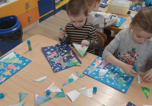 Dzieci przyklejaja wyciete trójkaty na kartkę.