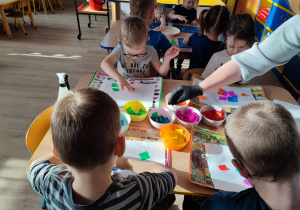 Dzieci układaja na białej kartce kolorowa bibułę.