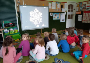 Dzieci oglądają zdjęcia płatków śniegowych na tablicy multimedialnej.