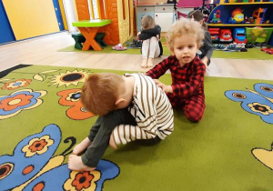 Zabawa "Kamień"- chłopiec próbuje przepchnąć kolegę, siedzącego na dywanie.
