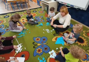 Dzieci siedzą na dywanie i drą papier na małe kawałki.