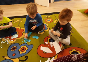 Dzieci siedzą na dywanie i drą papier na małe kawałki.