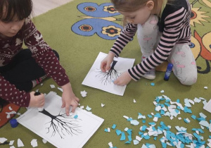 Dzieci kawałkami papieru wyklejają gałązki drzewa.