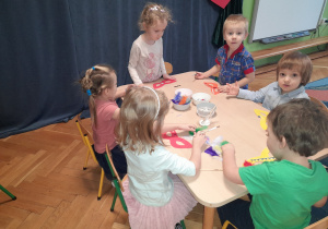 Dzieci siedzą przy stoliku i wykonują maski karnawałowe.