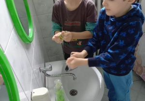 Dzieci piorą skarpety przy umywalkach.