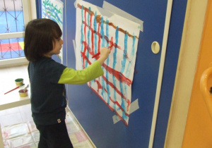Chłopiec maluje farbami na dużym arkuszu papieru.