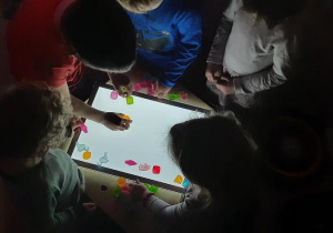 Dzieci układają kolorowe kostki lodu na panelu świetlnym.