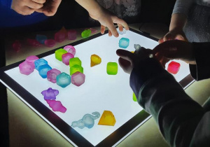 Dzieci układają kolorowe kostki lodu na panelu świetlnym.