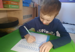 Chłopiec pisze szlaczki.
