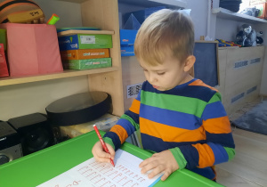 Chłopiec pisze szlaczki po śladzie.