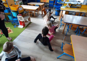 Dzieci z uniesionymi nogami na podłodze kręcą się dookoła siebie.
