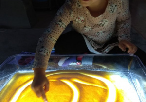 Chłopiec rysuje palcem w kaszy mannie na podświetlonym panelu.