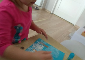 Dziewczynka maluje farbami na bombelkowej folii.