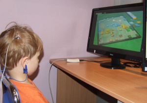 Dziecko siedzi przed monitorem, ma podłączone elektrody do głowy. Patrzy na zmieniający się obraz 