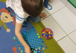 Chłopiec układa kamyki kolorowe na plastykowej podkładce.