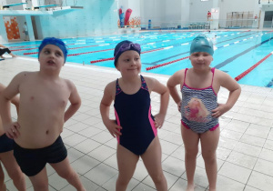 Trójka dzieci ćwiczy na brzegu basenu - rozgrzewka.